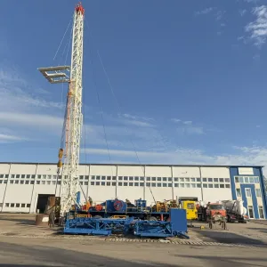 Oil drilling rig set up in front of a large industrial building under a blue sky.