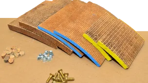 Four brown brake pads with bolts and washers on a  surface.