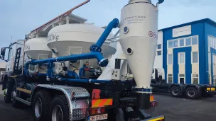 Truck carrying large white industrial tanks in a parking lot near a blue building.