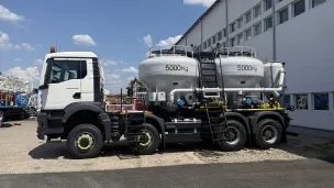White industrial truck with two large 500 kg tanks parked by a building.